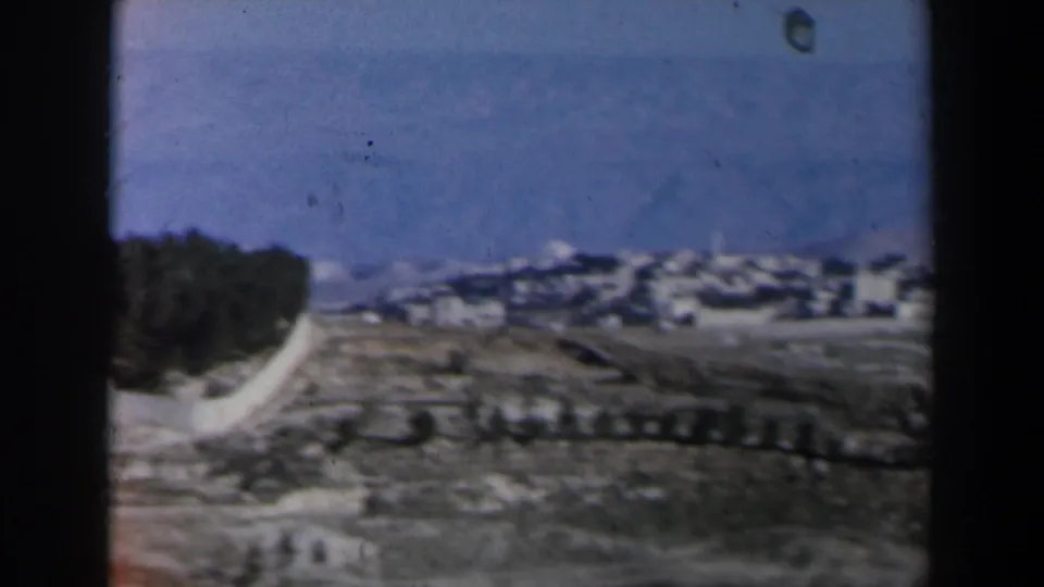 1960 Israel 8mm frame showing a low landscape view with distant pale buildings, sky, and a dark film border.