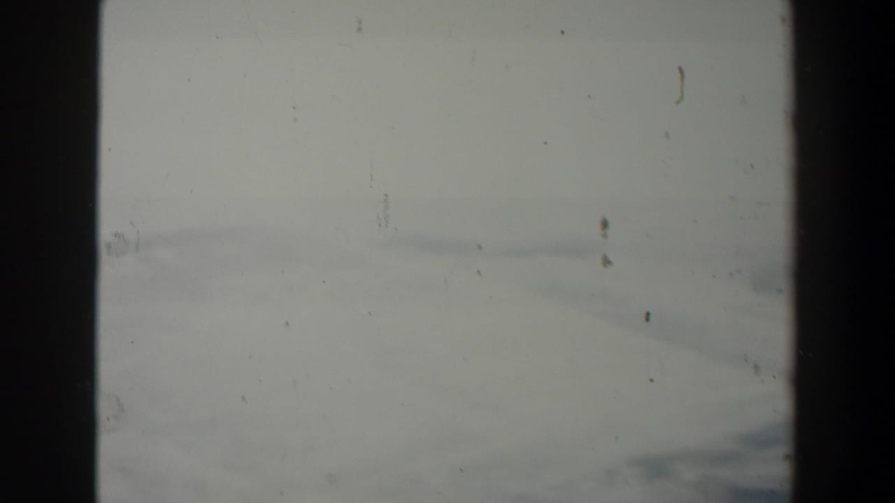 Hazy landscape seen through a dark vertical frame with dust and scratches across the film.