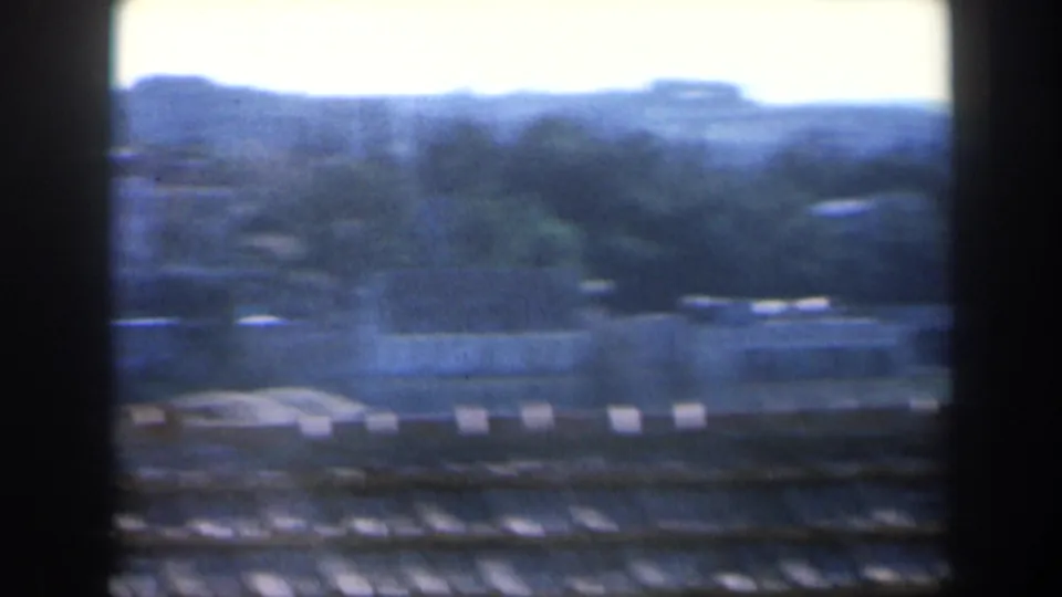 1960 Israel 8mm frame showing a tan shingled rooftop and distant low buildings against a hazy hillside.