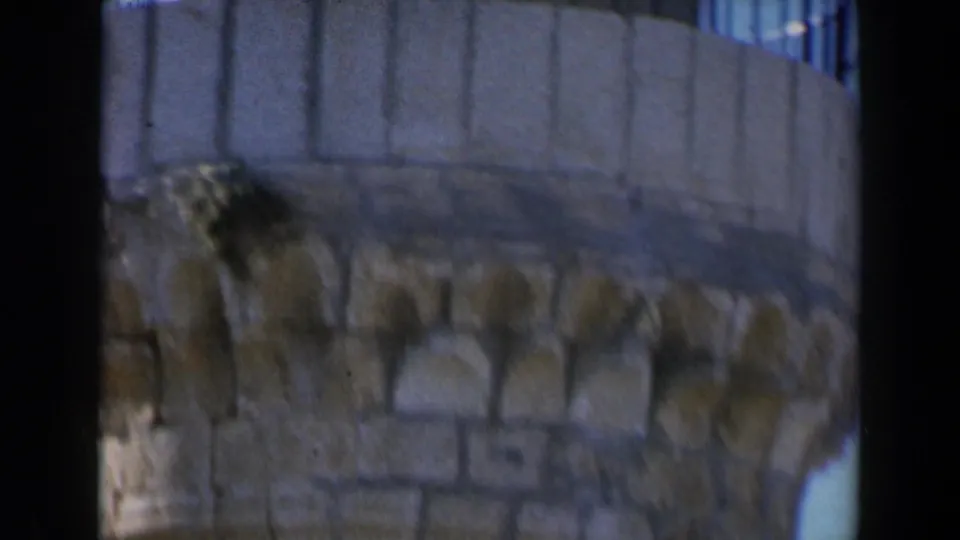 1960 Israel 8mm frame showing a close tan wall or tower edge with rooftop texture and blue-tinted film softness.