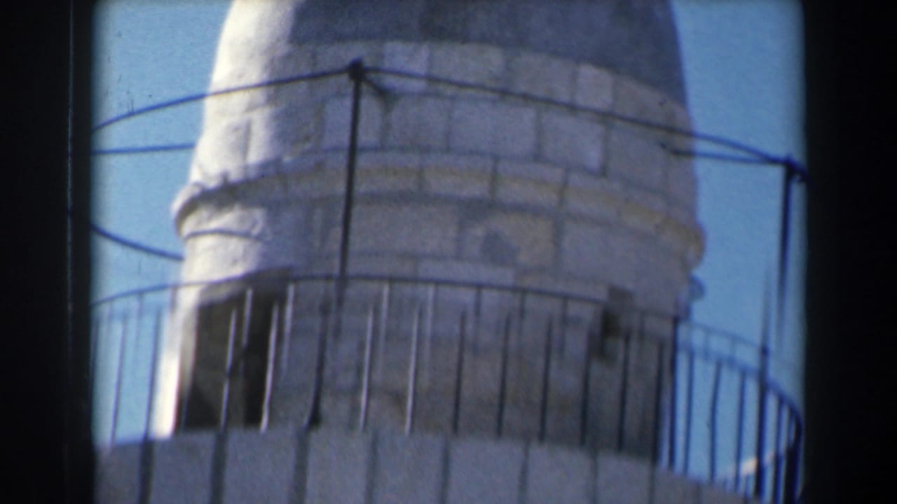 Close view of a pale stone tower section with metal railing against blue sky.
