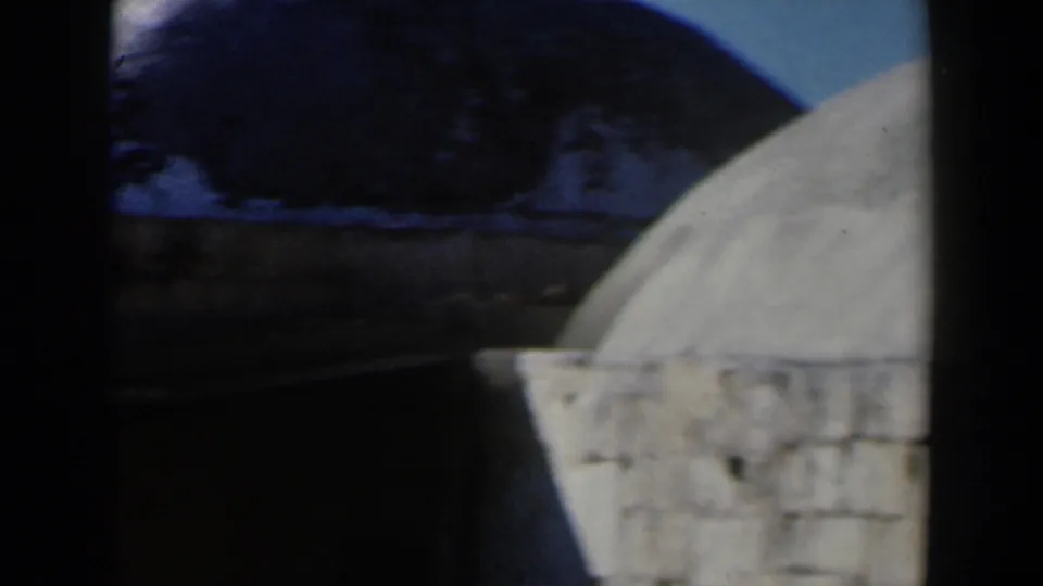 1960 Israel 8mm frame showing a pale stone dome, darker rooftop shapes, and part of a stone tower at the right edge.