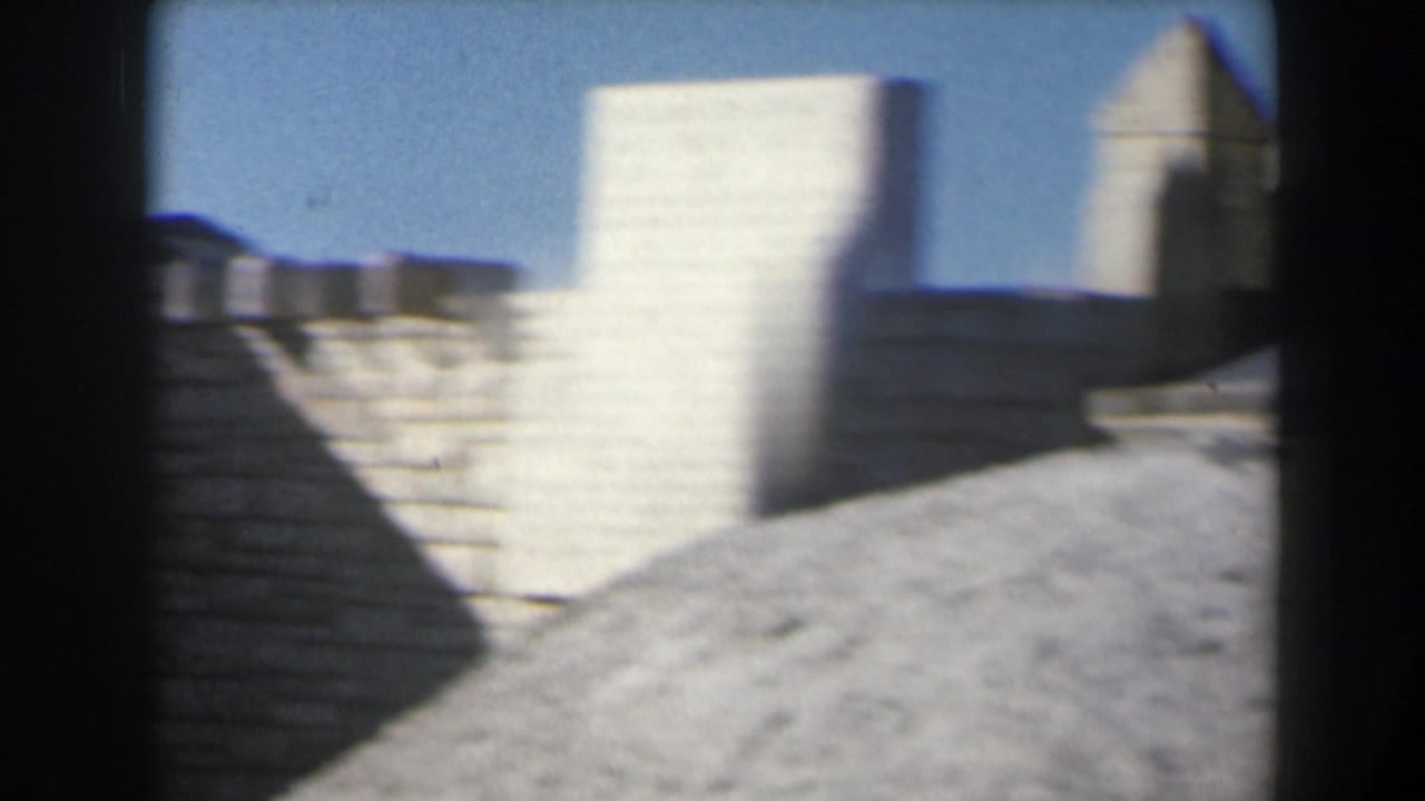 1960 Israel 8mm frame of sunlit stone architecture with stepped walls, a rectangular tower form, and open blue sky.