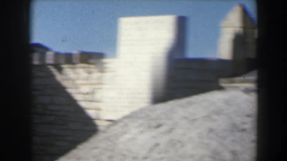 1960 Israel 8mm frame of sunlit stone architecture with stepped walls, a rectangular tower form, and open blue sky.