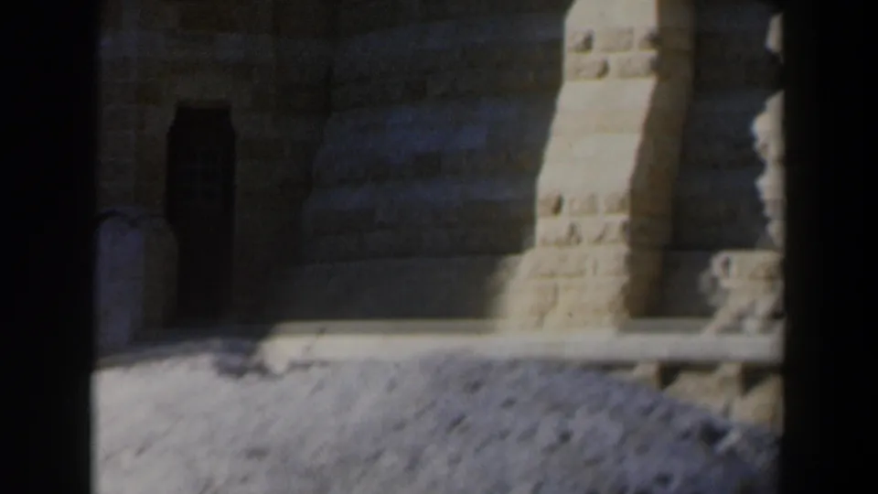 1960 Israel 8mm frame showing a close stone facade with a dark doorway, textured masonry, and sunlit ground.