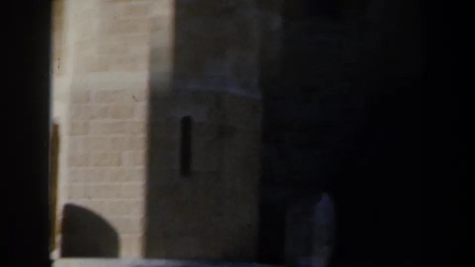 1960 Israel 8mm frame of a tall pale stone wall with a small arched opening, strong shadow, and adjacent masonry.