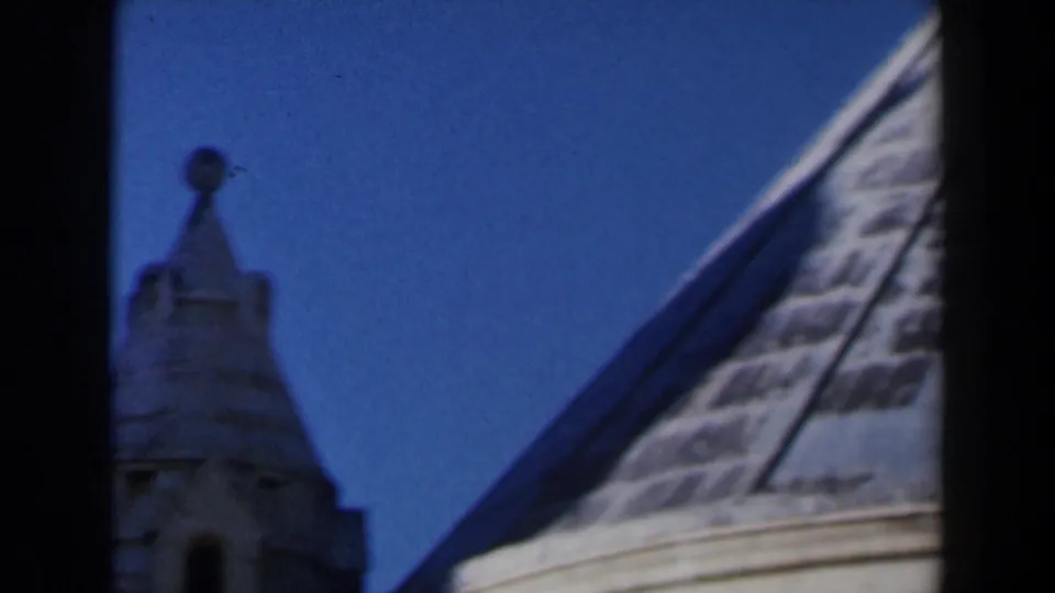 1960 Israel 8mm frame looking up at a small stone turret and sloped roofline against deep blue sky.