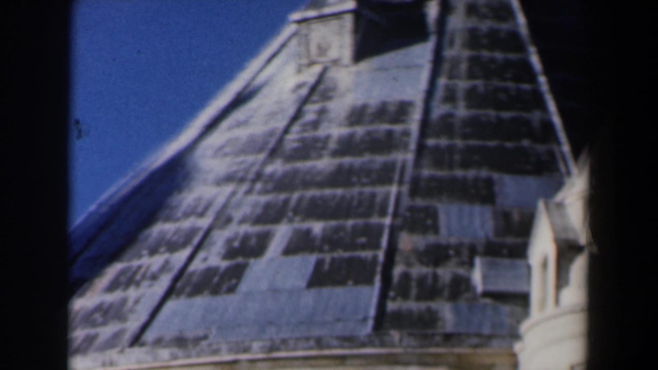 1960 Israel 8mm frame showing a steep weathered church or cathedral roof with pale turret details against clear blue sky.