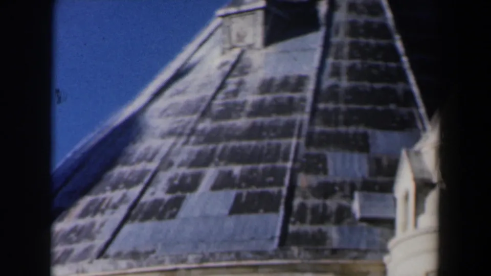 1960 Israel 8mm frame showing a steep weathered church or cathedral roof with pale turret details against clear blue sky.