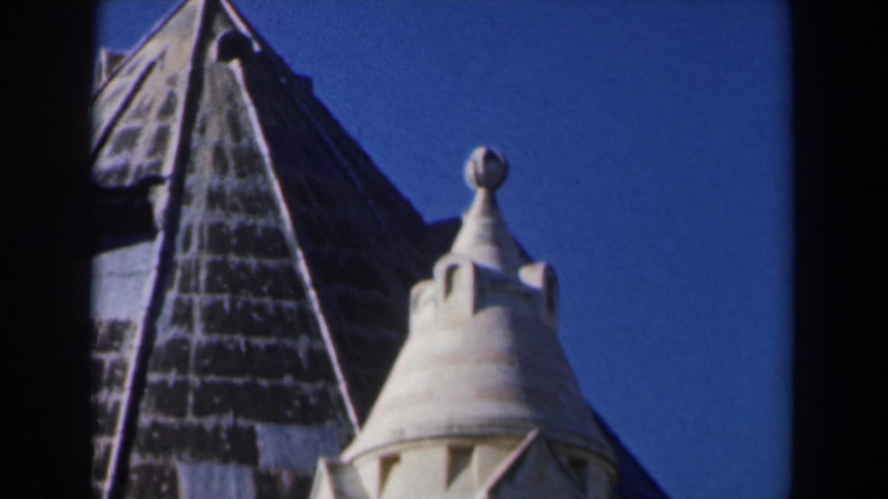1960 Israel 8mm frame with a dark roof peak, pale spire, finial, and blue sky in a close architectural view.