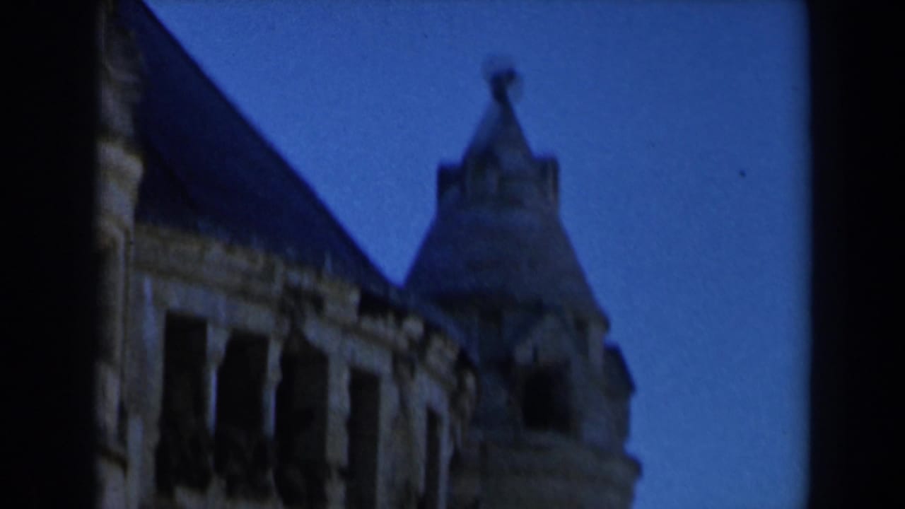 1960s Israel home-movie frame showing part of a historic stone structure with a dark roofline, tower form, and open arched windows.