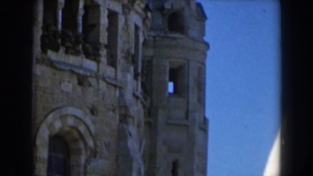 1960s Israel frame showing a stone tower section with an arched opening, rough masonry, and bright blue sky beside the structure.