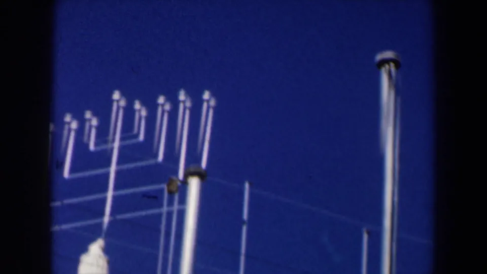1960s Israel home-movie frame showing metal flagpoles or rooftop fixtures against a deep blue sky near the stone structure.
