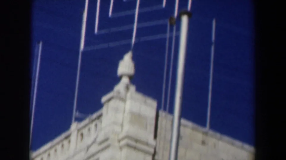 1960 Israel 8mm frame showing a white stone building roofline, vertical poles, and a small silver roof object against blue sky.