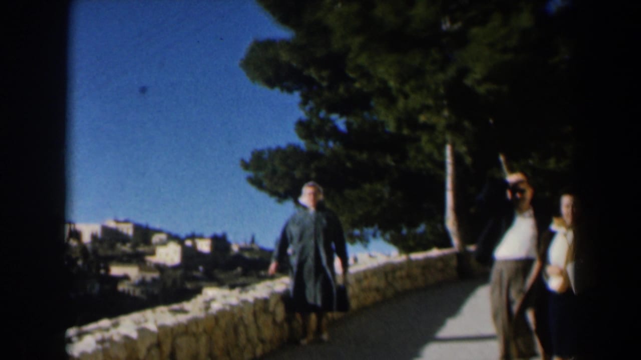 A color 8mm frame from Israel in 1960 shows pedestrians on a bright path beside stonework and dark green trees.