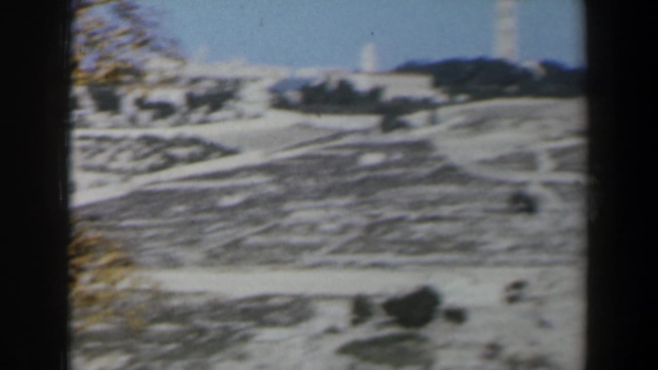 Distant white tower above stone terraces and scattered trees under a hazy sky.