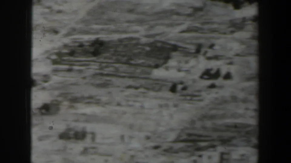Grainy 1960 Israel home-movie frame of terraced stone terrain with sparse vegetation and indistinct distant forms.