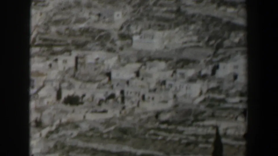 1960 Israel 8mm frame with distant low buildings, stone terraces, hillside contours, and dark gate edges.
