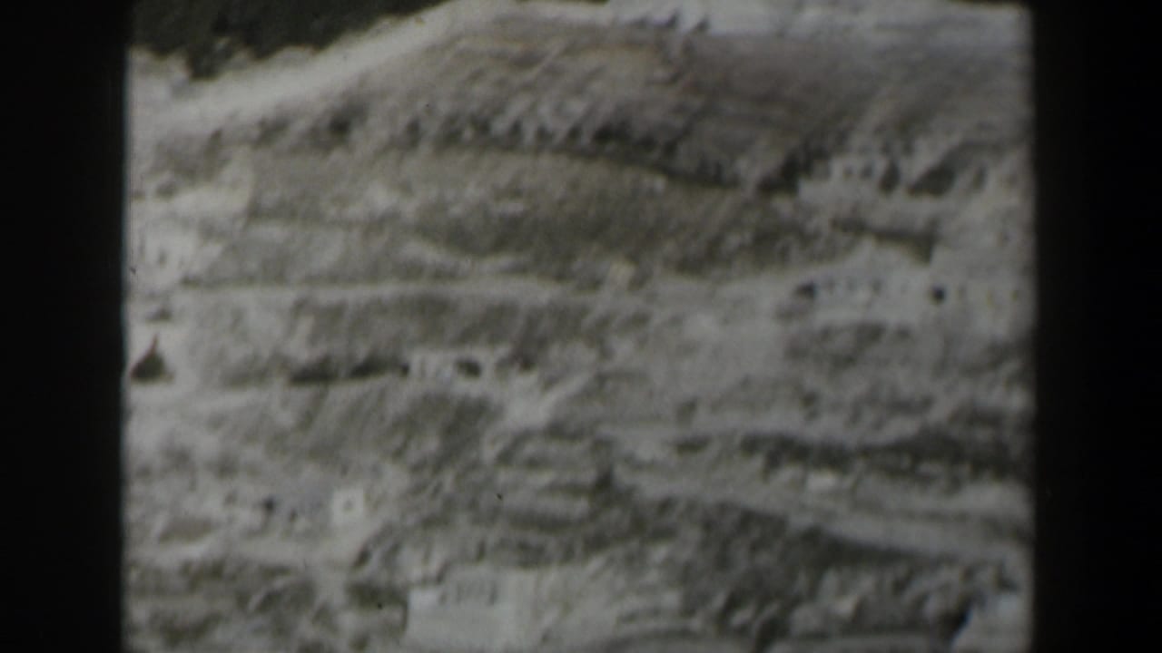 1960 Israel 8mm frame of an arid mountain slope with scattered light-colored structures and visible film gate edges.