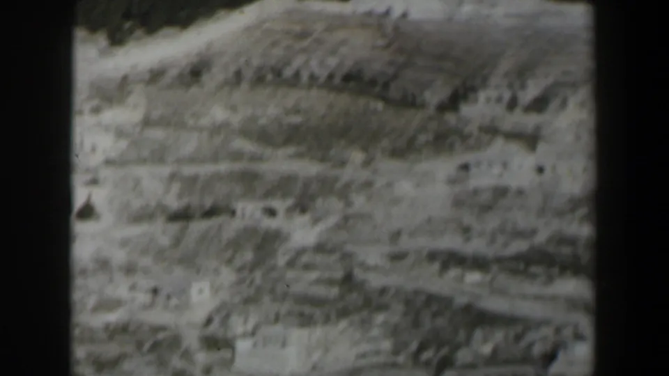 1960 Israel 8mm frame of an arid mountain slope with scattered light-colored structures and visible film gate edges.