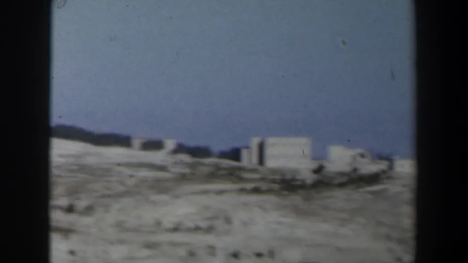 1960 Israel 8mm frame showing a large white building complex on an arid ridge under a clear blue sky.