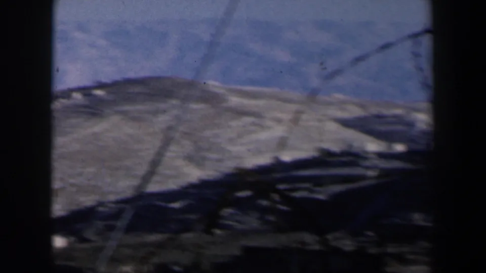 1960 Israel 8mm frame showing pale brown desert mountains and blue sky, partly obscured by dark window or vehicle-frame edges.