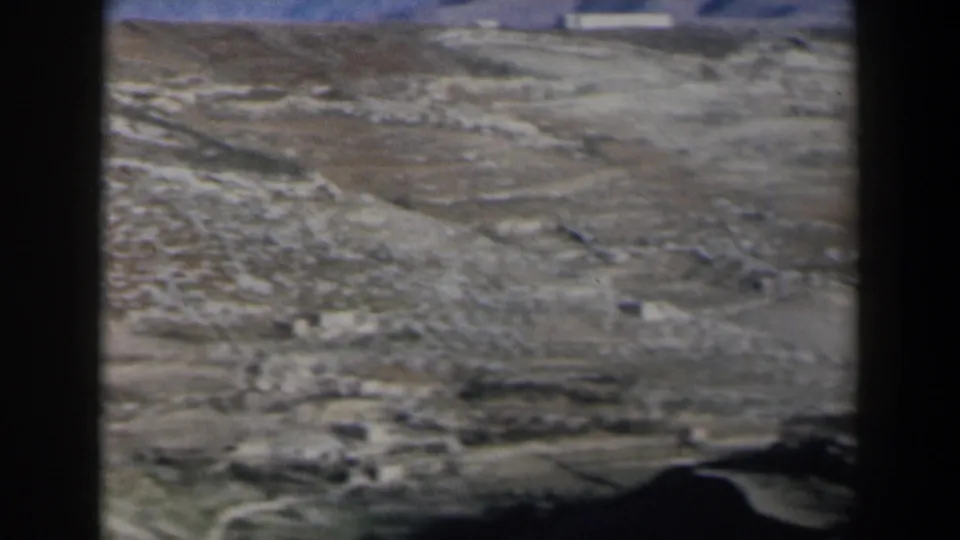1960 Israel home-movie frame showing rocky desert ground, pale brown hills, and a soft blue sky with dark edge shadow.
