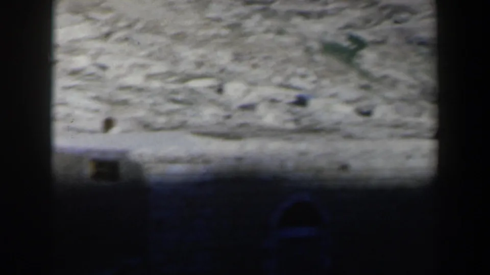 1960 Israel 8mm frame showing a pale desert hillside, dark foreground framing, and a small greenish area in the arid terrain.