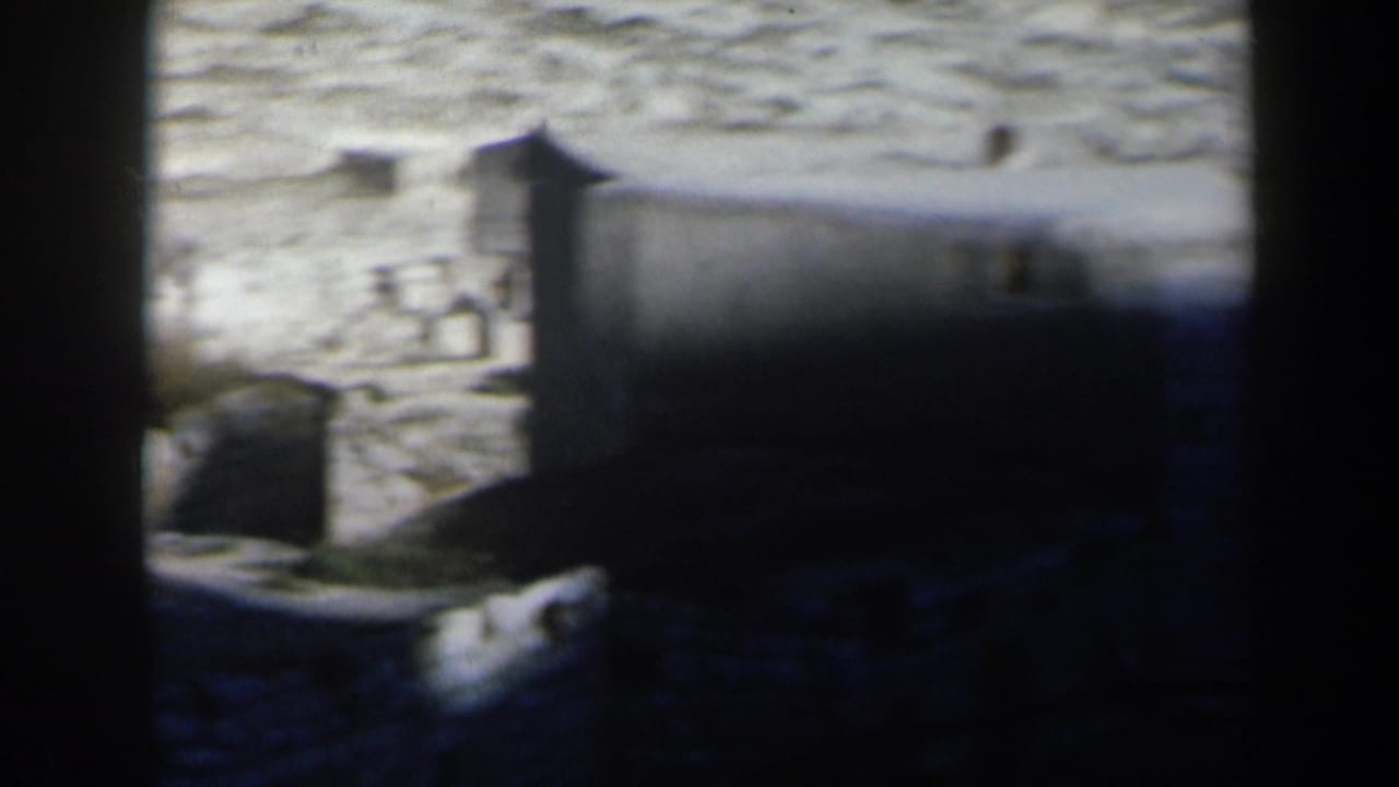 1960 8mm home-movie view in Israel showing pale hillside structures seen through dark foreground framing.