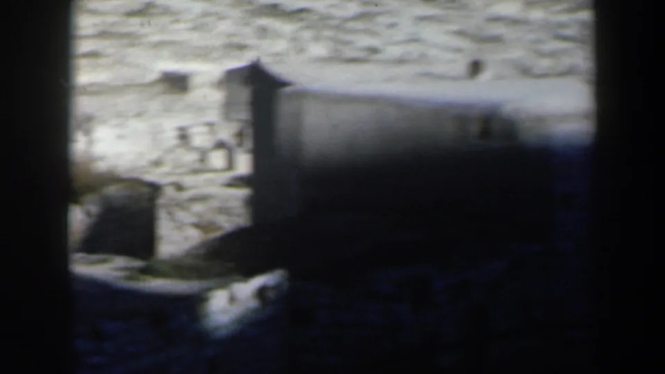 1960 8mm home-movie view in Israel showing pale hillside structures seen through dark foreground framing.