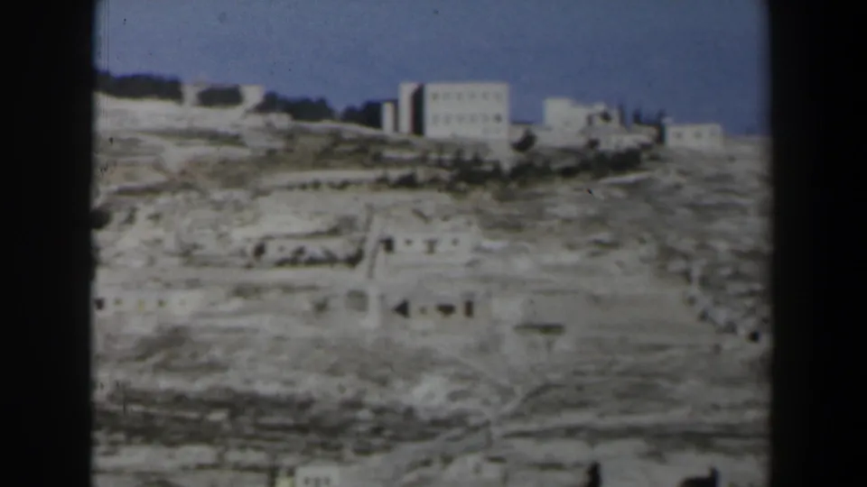 1960 Israel home-movie frame showing distant hilltop buildings above a pale rocky slope and clear blue sky.
