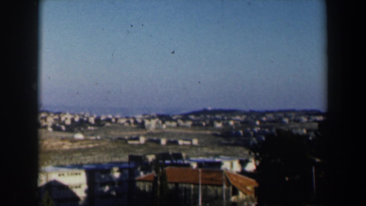 Panoramic view of a hillside town seen past dark balcony framing.