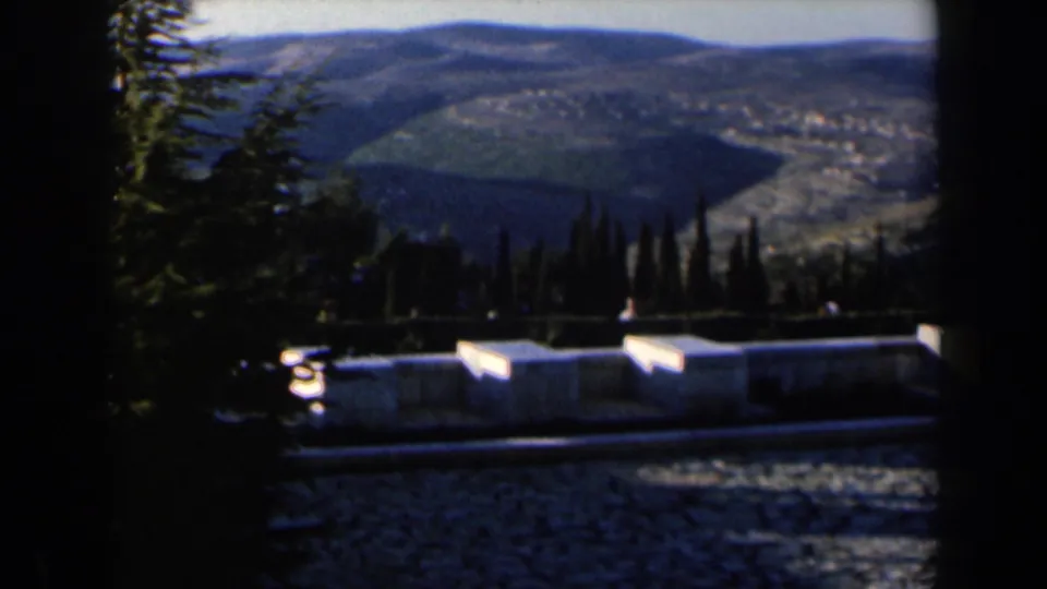 The camera looks over a stone wall toward trees, fields, and rounded hills in Israel home-movie footage from 1960.