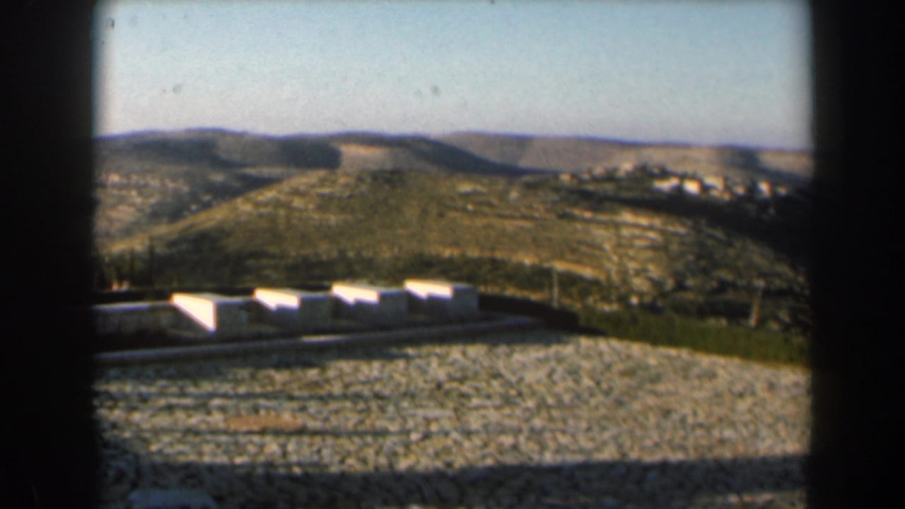 1960 Israel landscape with low white foreground structures, arid hills, and a distant cluster of buildings.