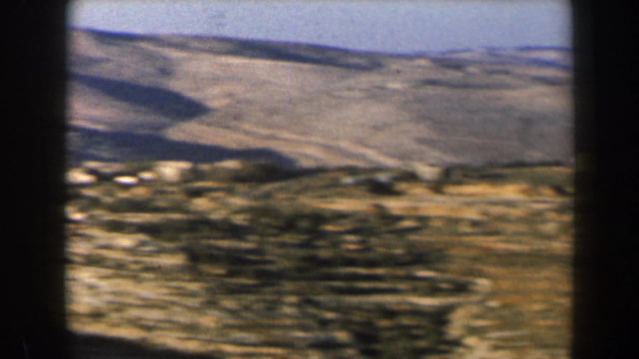 Arid hills with scattered pale buildings and dark film-frame borders.