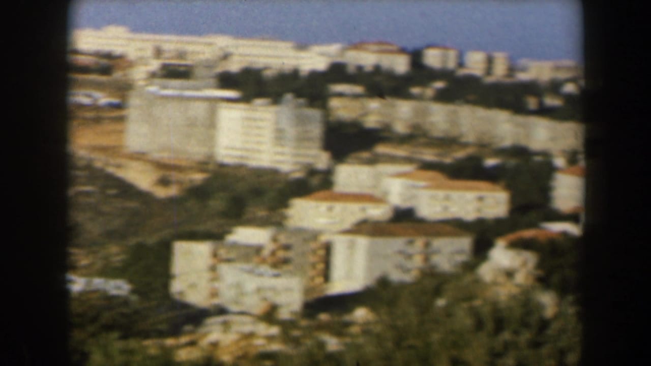 1960 Israel home-movie view of white hillside buildings, red roofs, trees, and blue sky from a distant overlook.