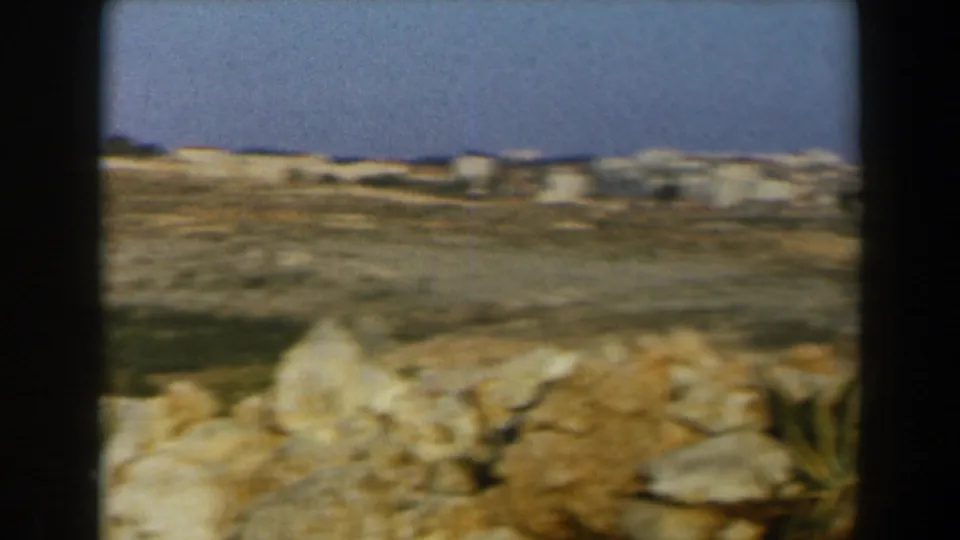 1960 Israel overlook showing rocky ground in the foreground and distant pale buildings across a dry hillside.