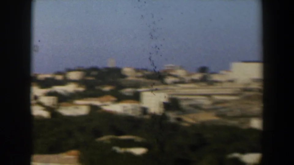 Soft 8mm view of white hillside buildings and open terrain in Israel, with the camera panning across the town.