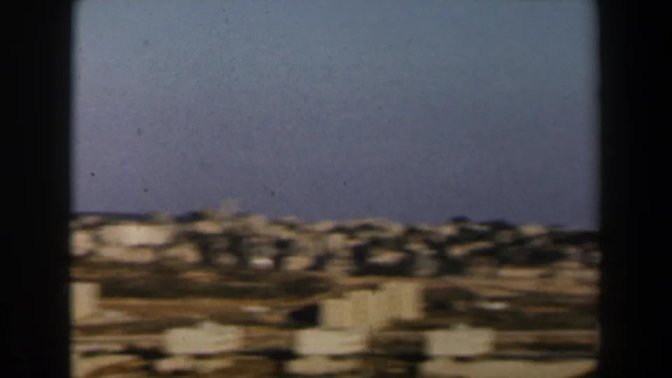 End of the 1960 Israel panorama, with distant white buildings, trees, dry terrain, and soft 8mm motion blur.