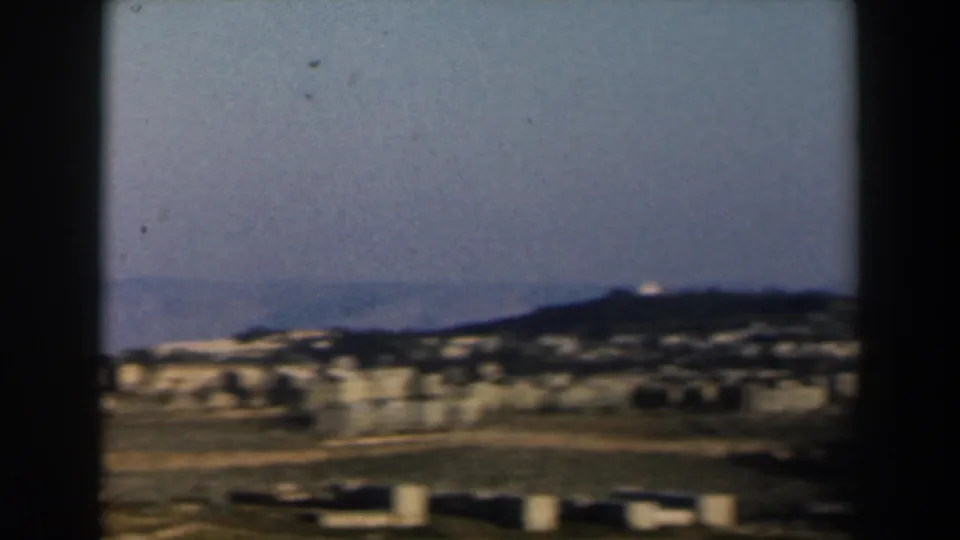 1960 Israel home-movie still showing low buildings, open terrain, and a dark ridgeline during the panorama.