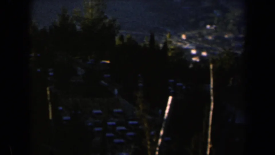 1960 Israel home-movie frame with shadowed trees in the foreground and pale hillside buildings beyond.