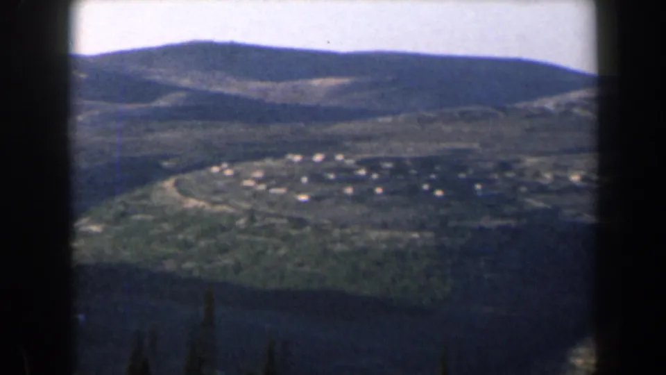 1960 Israel 8mm landscape frame showing clustered valley buildings, hills, and dark foreground tree shapes.