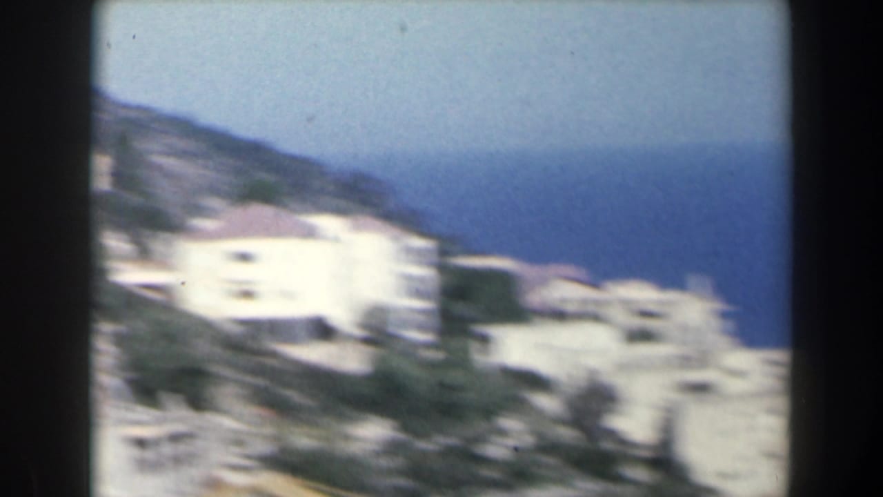Blurred white hillside buildings above a blue Mediterranean shoreline.