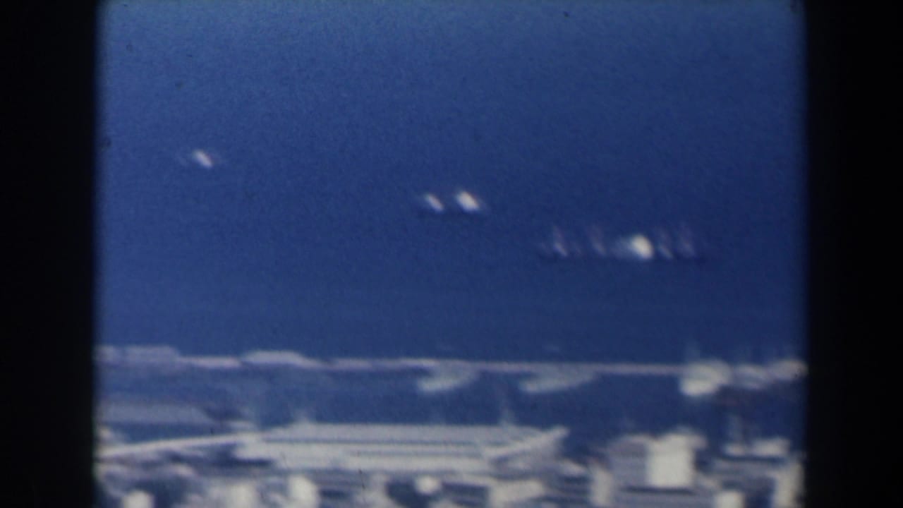 1960 Israel 8mm frame with small distant vessels on blue harbor water beyond low coastal structures.