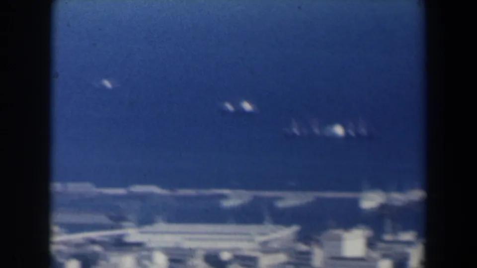 1960 Israel 8mm frame with small distant vessels on blue harbor water beyond low coastal structures.