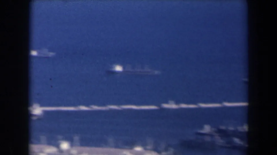 1960 Israel 8mm frame with boats, a visible wake, and low coastal land across blue harbor water.