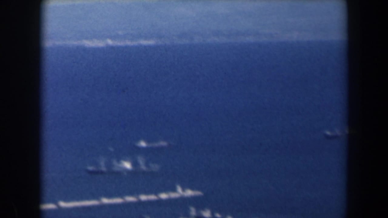 Open blue water with distant shoreline, small vessels, and dark vertical frame bars.