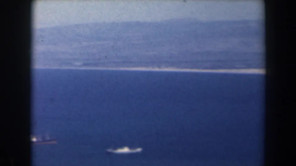 1960 Israel 8mm aerial view of a pale coastline, blue water, and small boats near the bottom of frame.