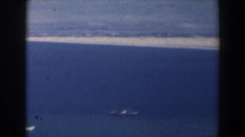 1960 Israel 8mm aerial view past dark window bars toward a hazy coast and small boats on the water.