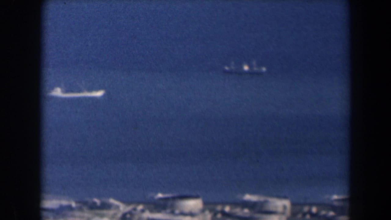 Distant ships on blue sea with a hazy shoreline below.